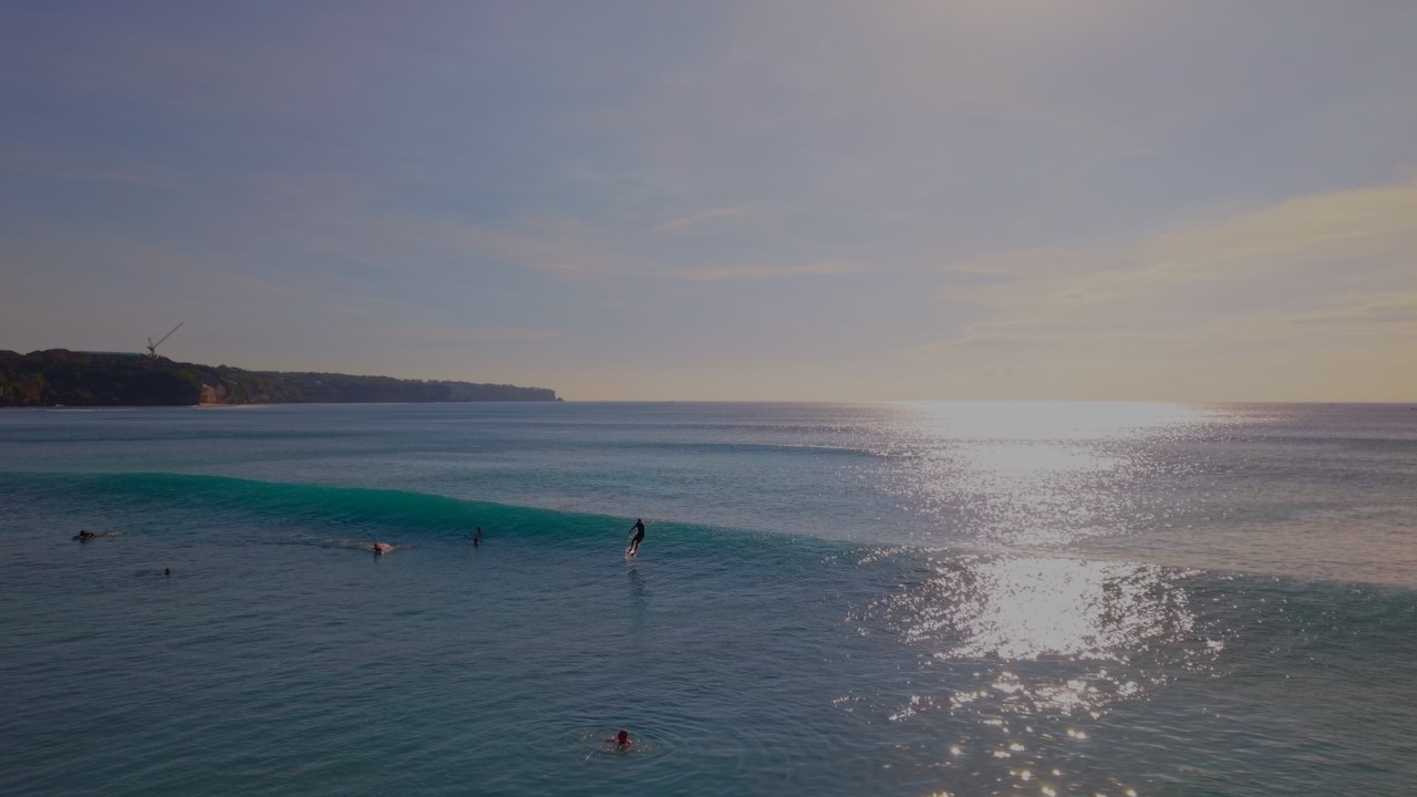 Aerial view of surfers riding a wave off the Bali coast at golden hour